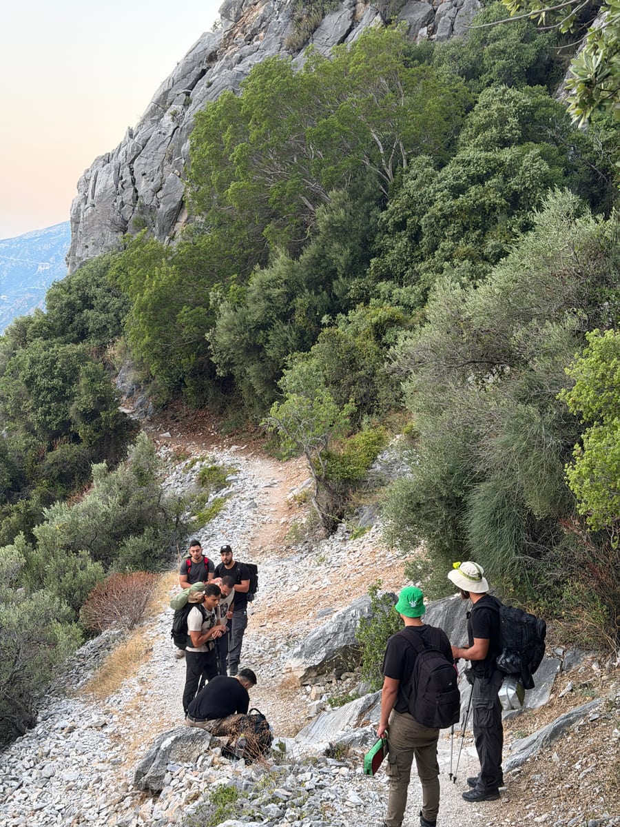A hiking group gathered on a rocky mountain path below a limestone cliff